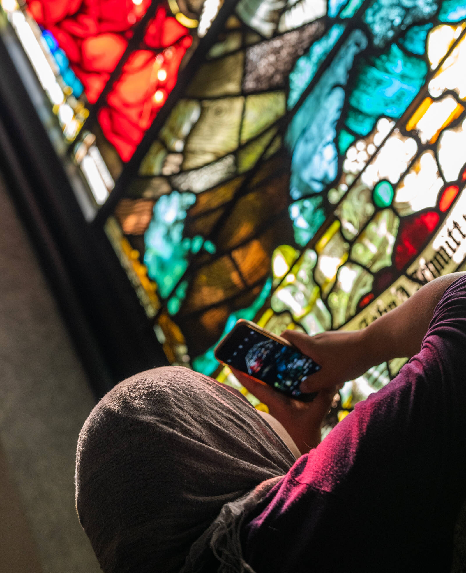 A girl in a head covering taking a close-up photo of a stained glass window